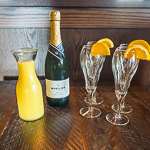 A carafe of orange juice, bottle of champagne, and 4 champagne flutes garnished with orange slices