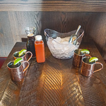 4 copper mule mugs garnished with limes, an ice bucket, ginger bier, and nonalcoholic spiced pineapple mix