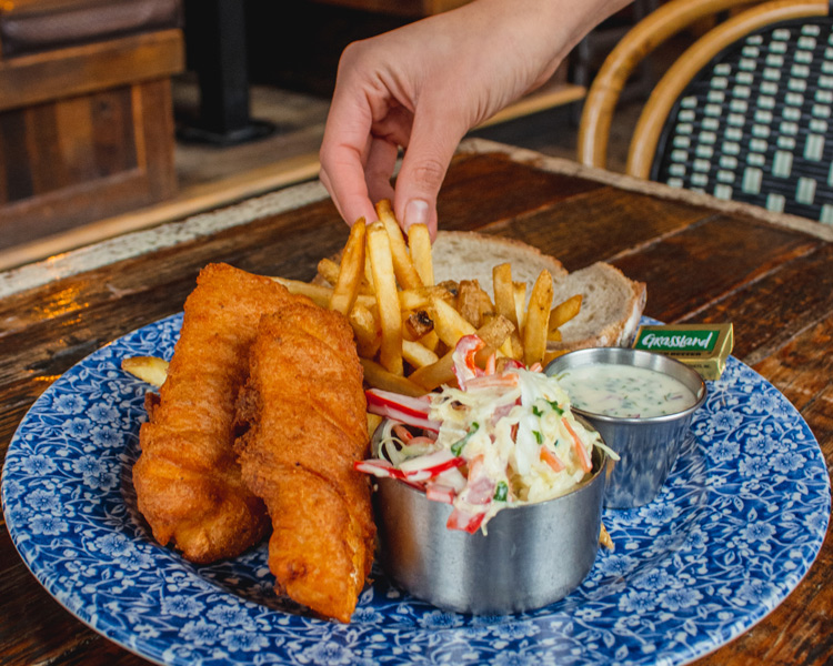 A hand reaching in to grab frites off of a Classic Fish Fry plate